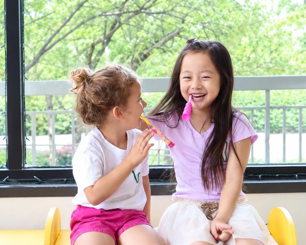 Two girls in La Petite Dent T-shirts laughing together on a yellow bench by the office windows
