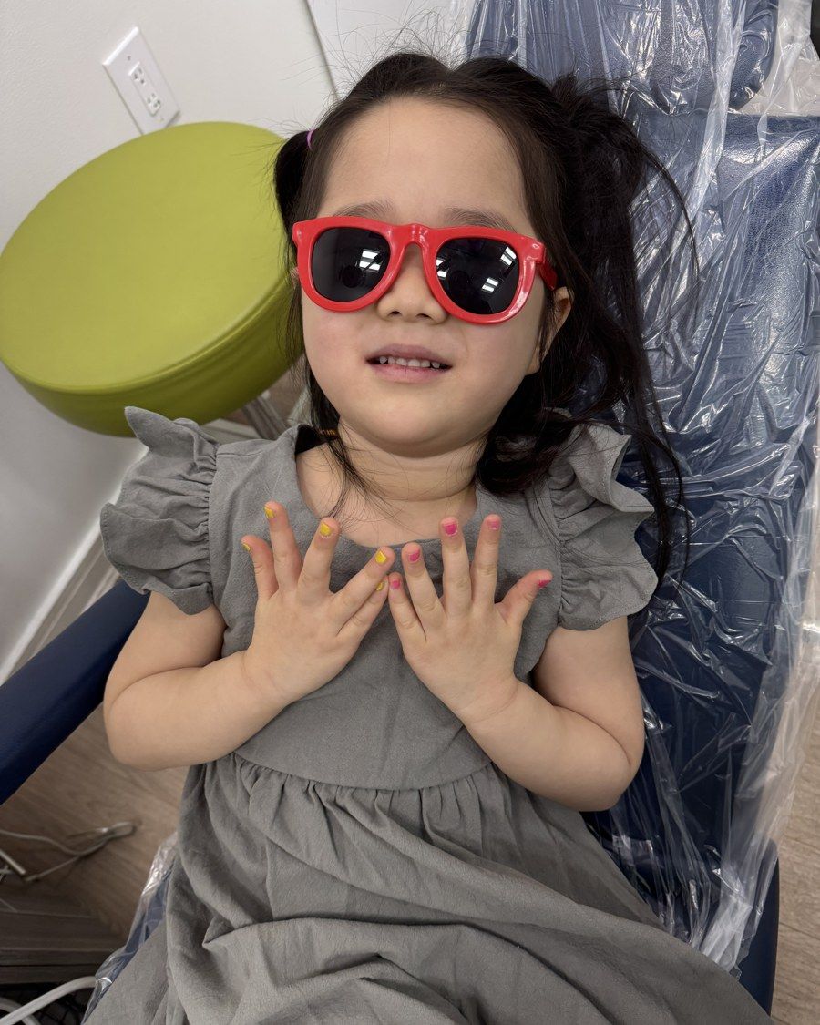 A young girl relaxing in the dental chair wearing red protective sunglasses